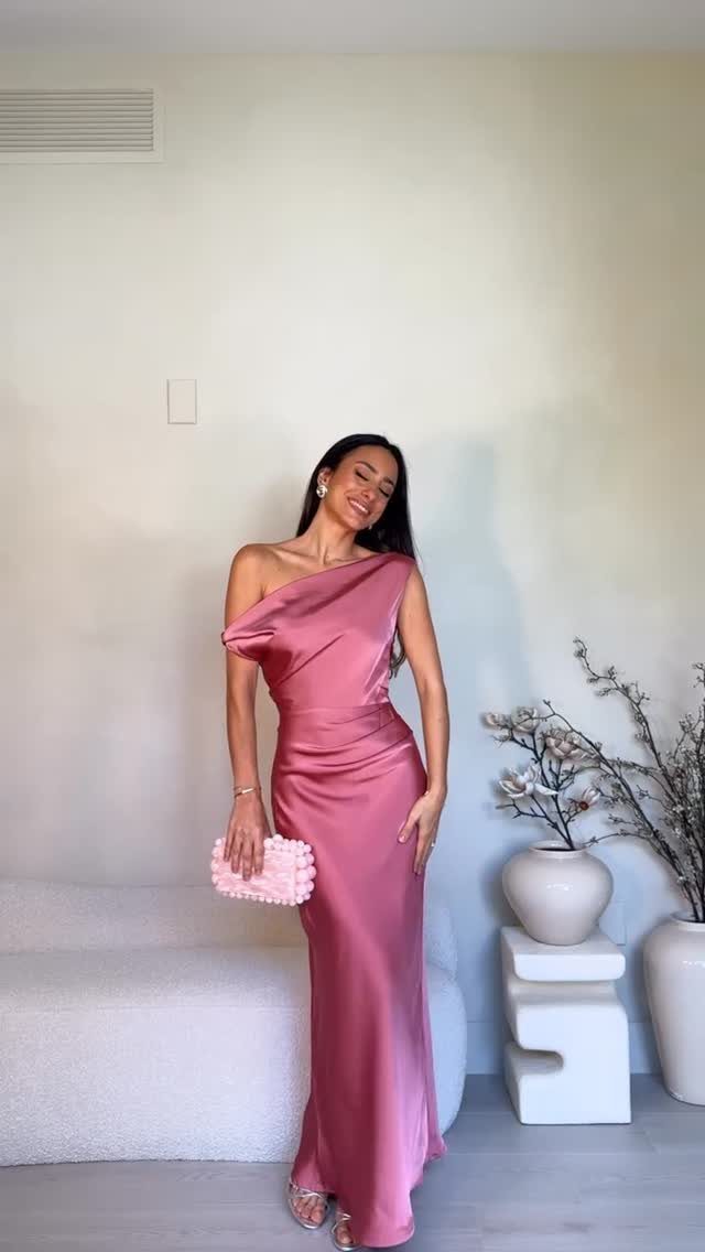 Woman wearing a pink satin one-shoulder maxi dress and holding a textured pink clutch.