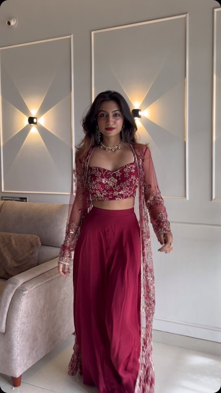 Woman in maroon sequined crop top, wide-leg trousers, and long sheer embroidered jacket.