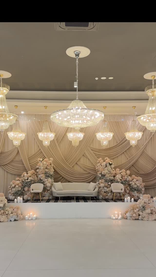 Blush and cream floral arrangements surround a white sofa on an elegant wedding stage.