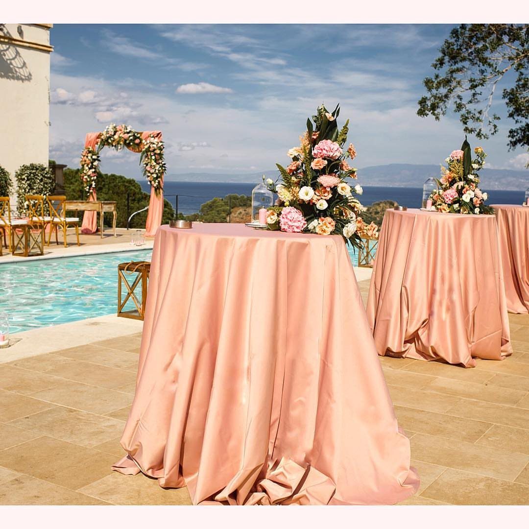 Dusty rose draped tables with floral arrangements overlooking a pool and the ocean.