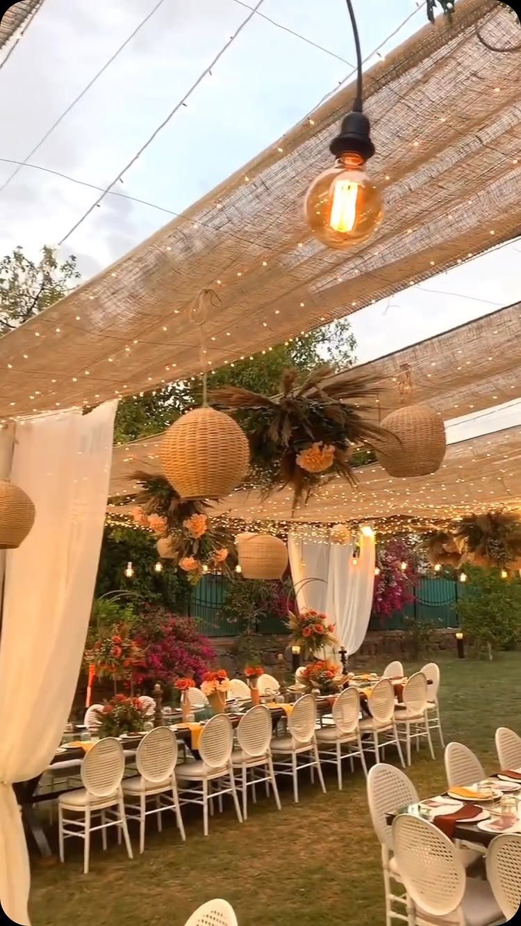 Outdoor wedding reception with burlap canopy, fairy lights, and hanging lanterns over dining tables.