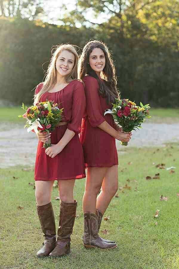 Two women in burgundy mini dresses and cowboy boots holding bouquets in a field.