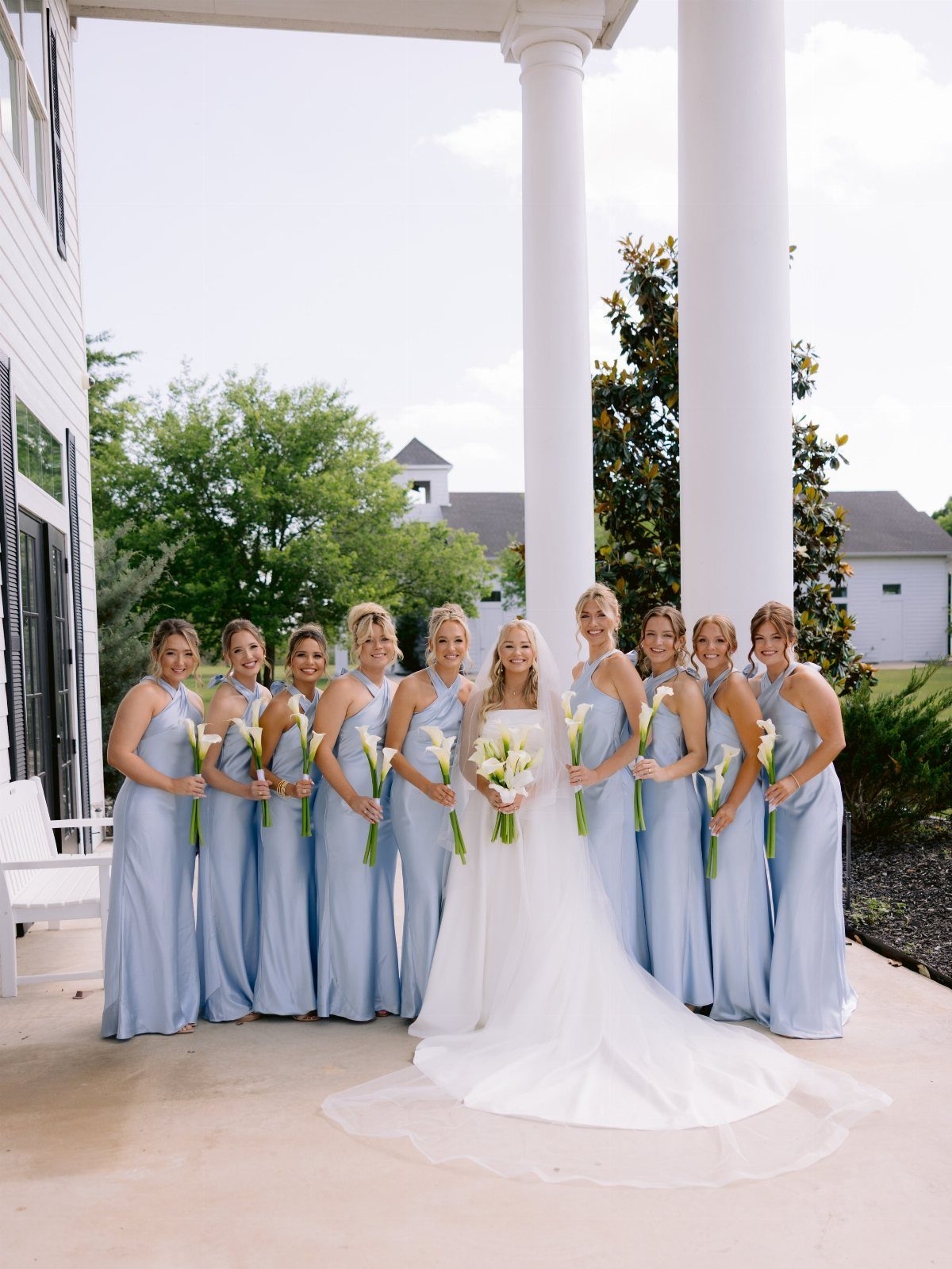 Bridesmaids in light blue halter-neck satin dresses stand beside a bride in a white gown.