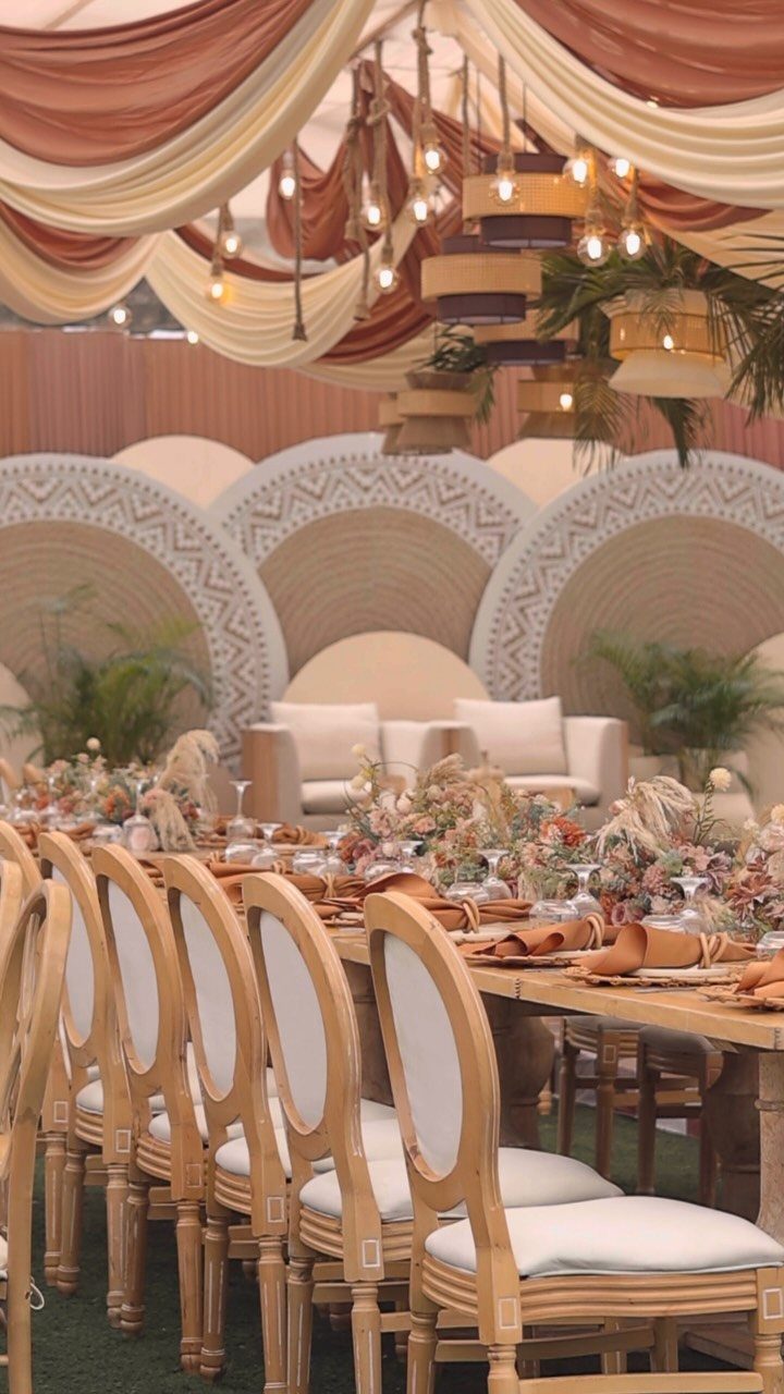 A long wooden dining table decorated with dried flowers and earthy-toned linens under draped fabric.