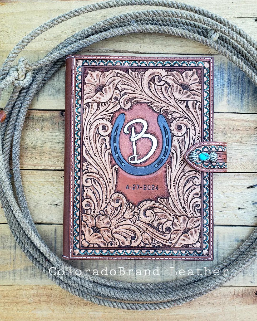 Tooled leather book with a horseshoe and letter B design surrounded by a coiled rope.
