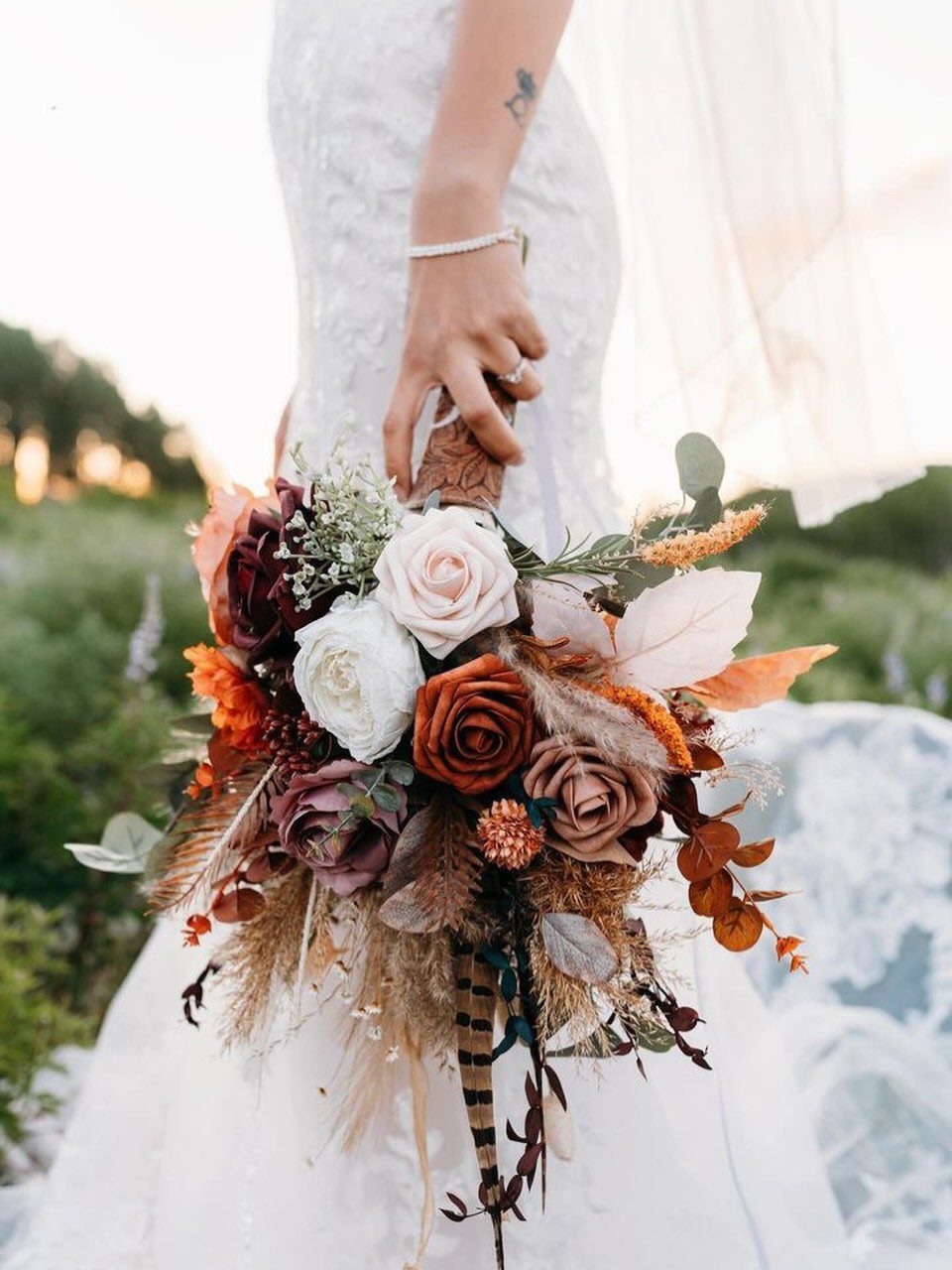 A bride holding a rustic bouquet with white and terracotta roses and dried foliage.