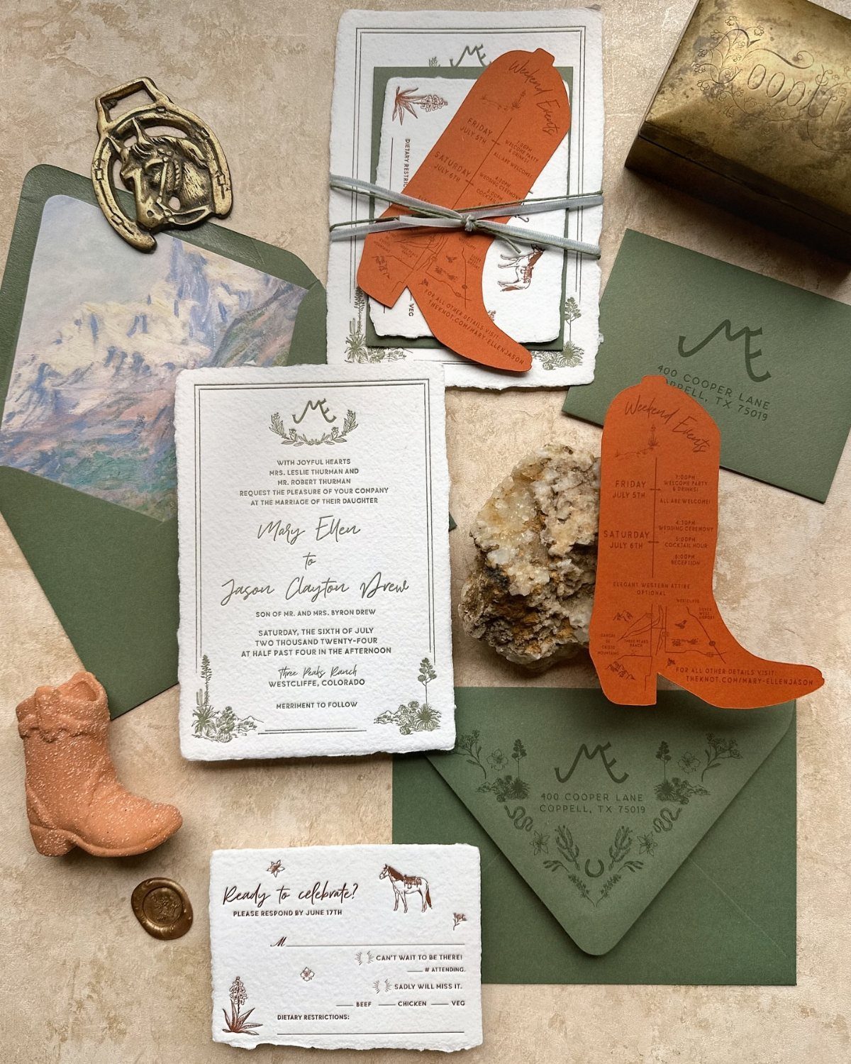 Western wedding invitations with boot-shaped cards and sage green envelopes arranged on a textured surface.