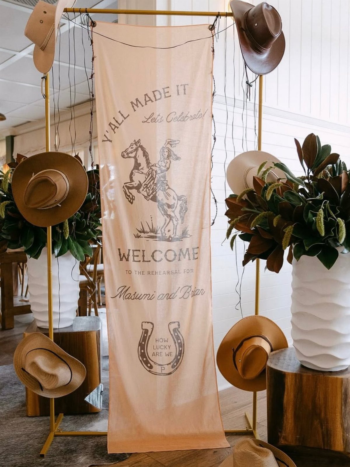 A tan welcome banner with cowboy graphics hanging on a gold frame decorated with cowboy hats.