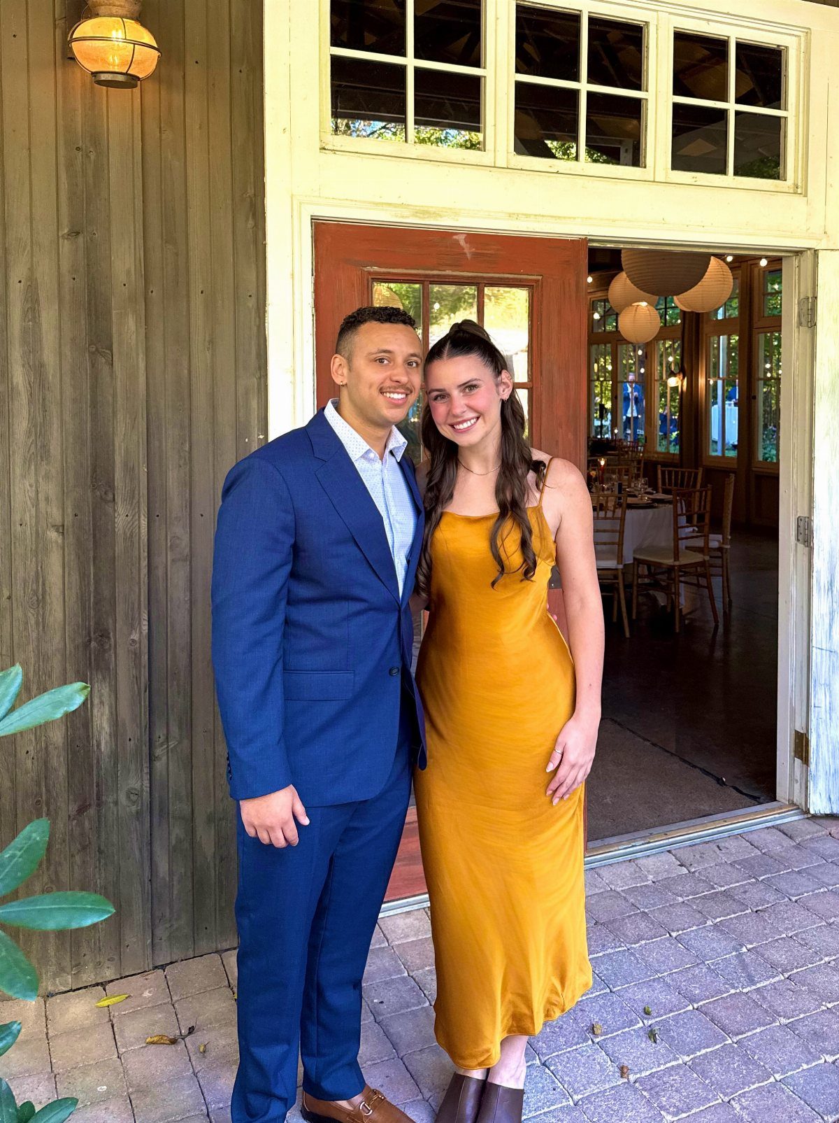 A man in a blue suit and a woman in a mustard yellow dress posing together.
