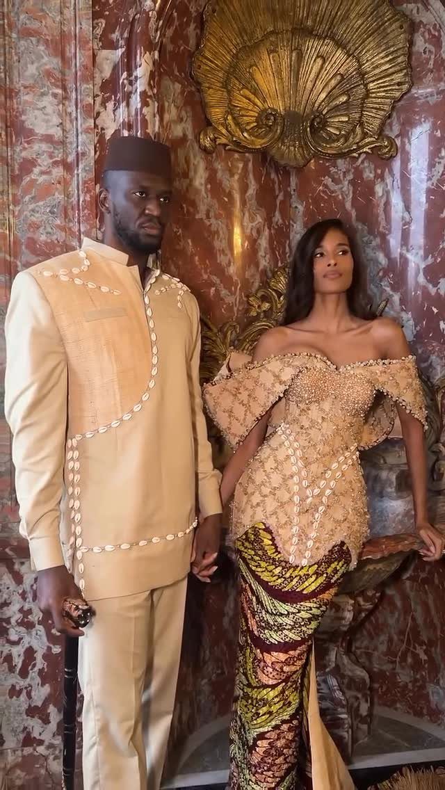 A man and woman posing in traditional African patterned clothing against a marble wall.
