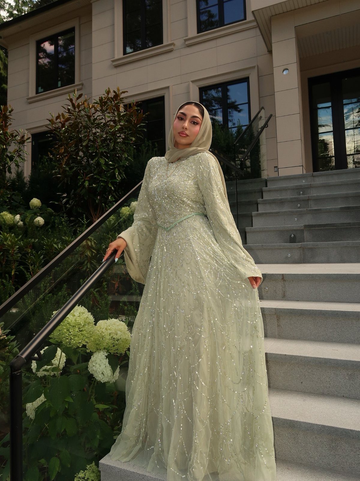 Woman in a long-sleeved light green sequined gown and matching hijab standing on stone stairs.
