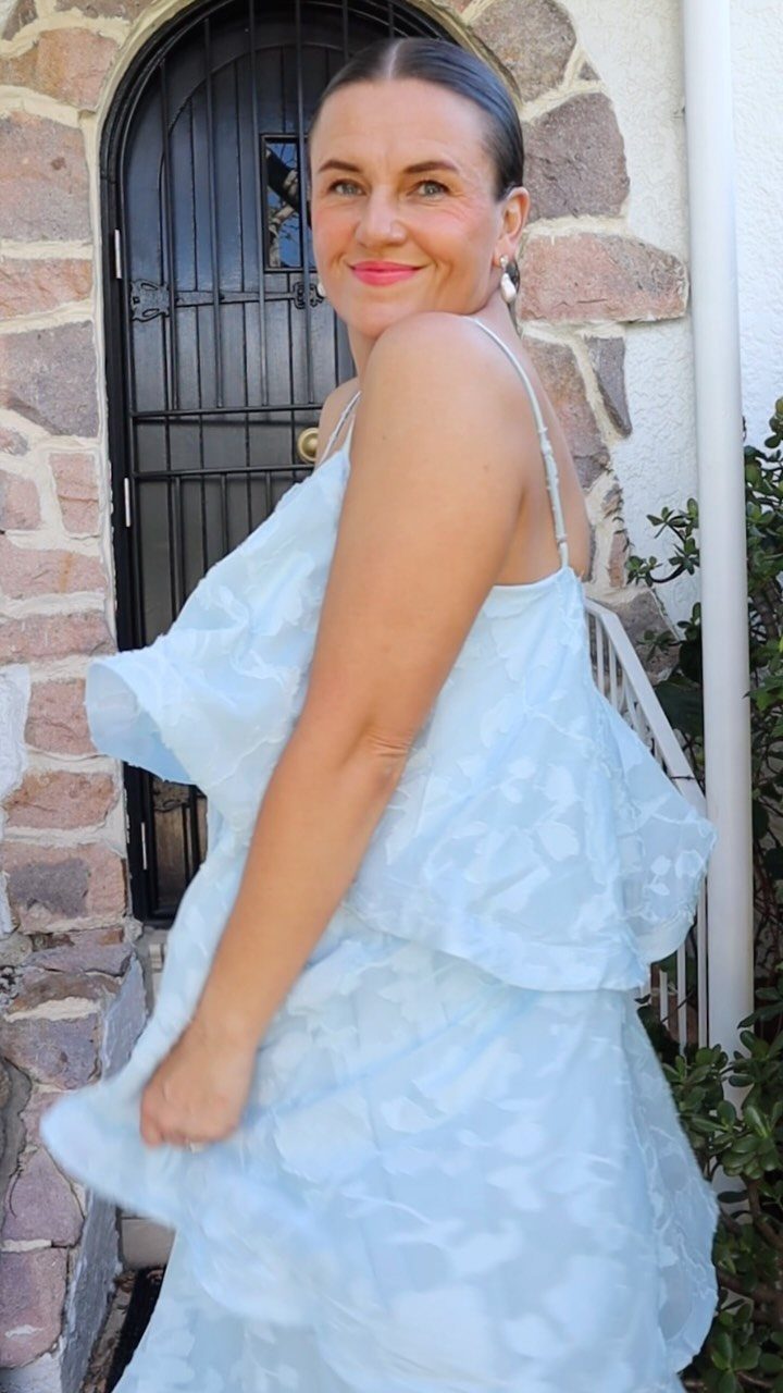 A woman in a light blue floral dress smiling while posing in front of a stone wall.