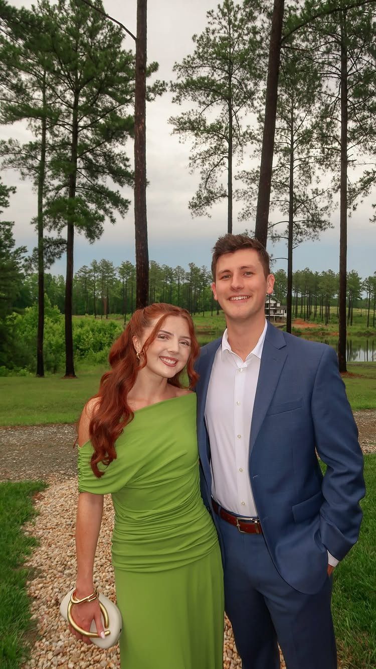A man in a blue suit and a woman in a green dress smiling outdoors.