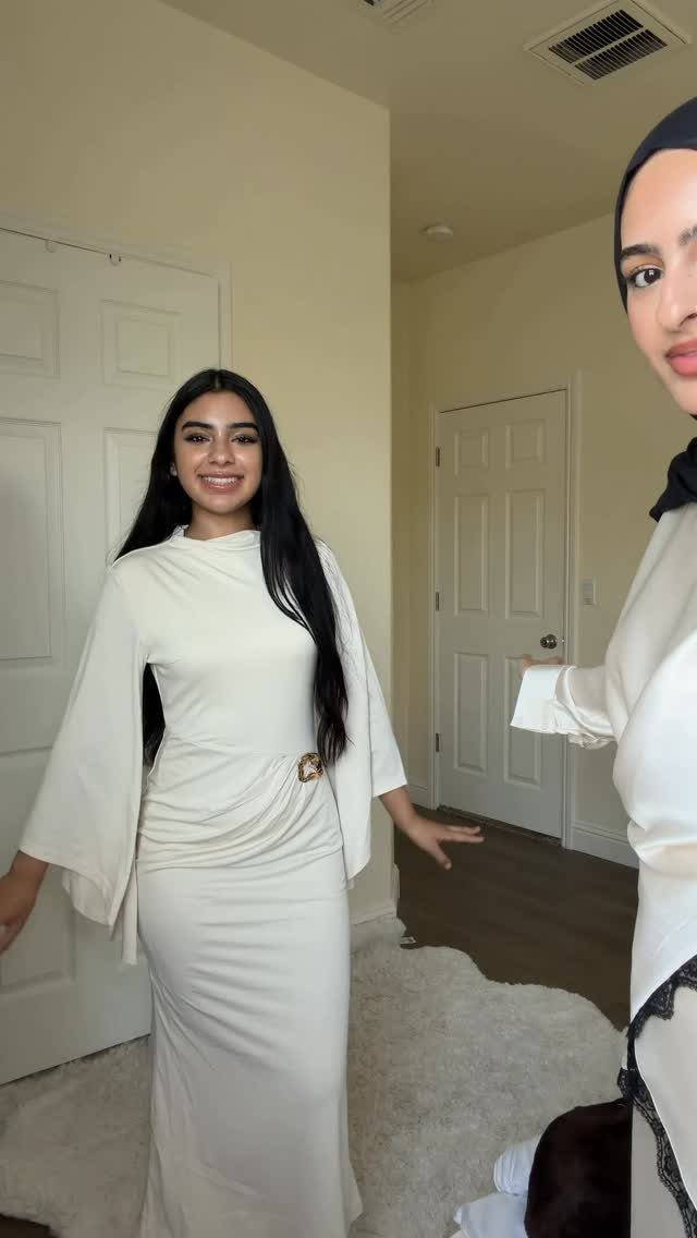 Smiling woman in a long cream bell-sleeved dress standing in a room.